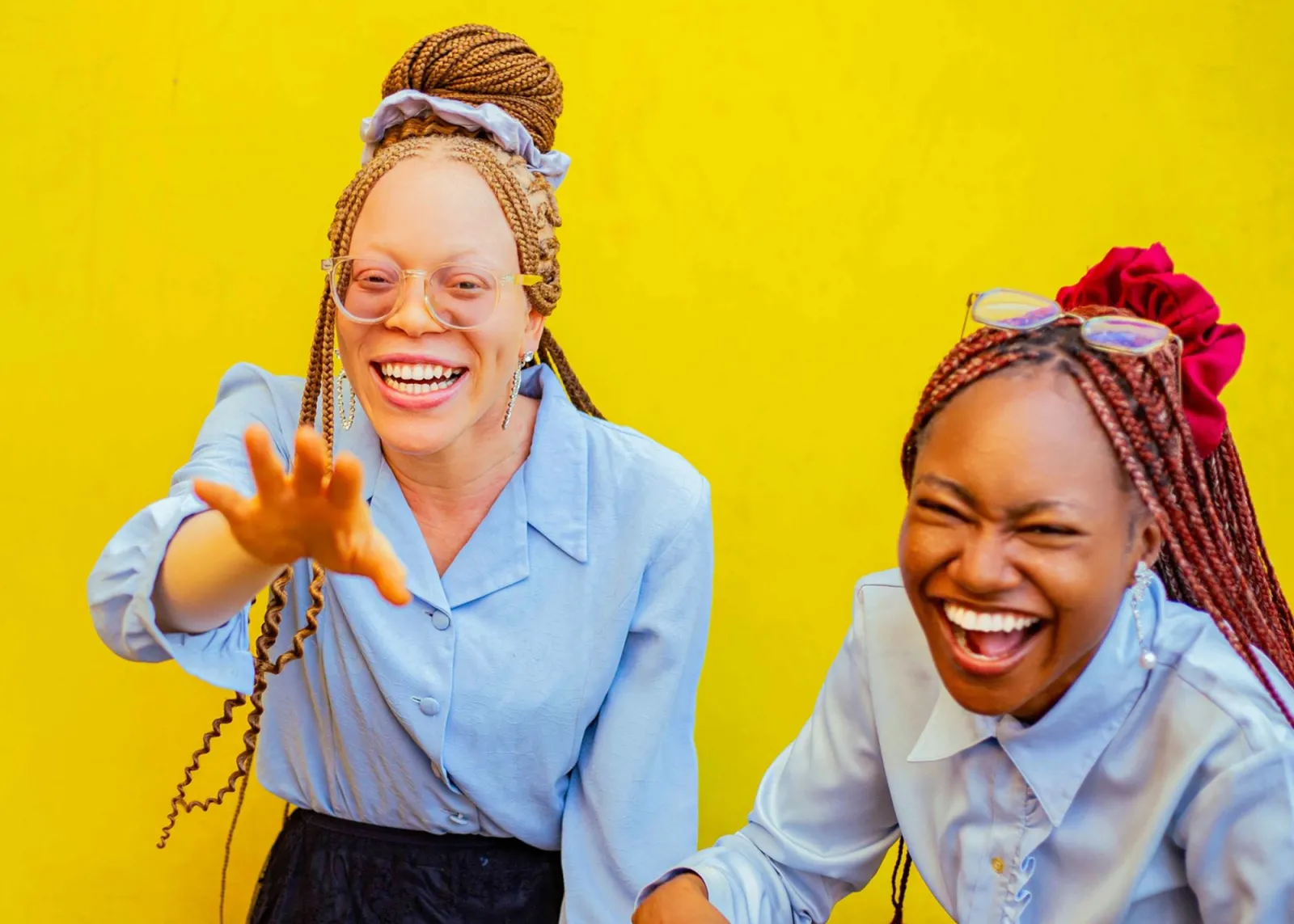 Two women laughing against a yellow backdrop